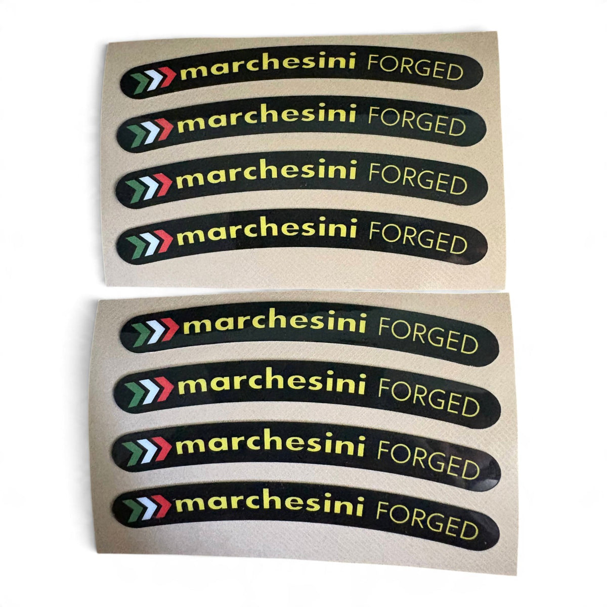 Two sheets of curved black stickers with the text 'marchesini FORGED' in yellow, each sheet containing five stickers. The stickers feature a multi-color chevron logo on the left.